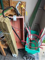 Photo of the gardening lot showing the 22-inch green spreader, Craftsman trimmer, wooden lawn stakes, turquoise resin flower baskets, and yellow hose extension wand.