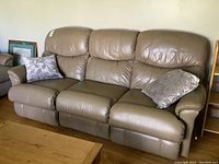 Full view of tan leather sofa with two decorative pillows.