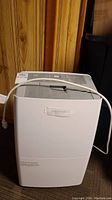 Front view of white Noma dehumidifier with power cord on top, showing control panel and vent.