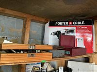 Shelf with Porter Cable hammer drill box and drill and sanding bits in wooden and metal cases.