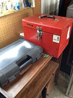 Red metal carrying case for Makita circular saw, sitting on wood surface