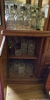 Top shelf of cabinet showing upside-down stemmed wine glasses and some drinking glasses behind