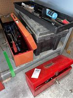 Two metal tool boxes, one red and one orange, stacked with a black resin tool box on top containing various tools.