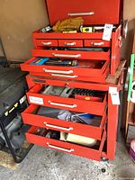 Red tool chest drawers open showing various tools and accessories including gloves and measuring tapes.