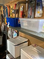 Shelf with plastic bins and boxes below, pegboard wall with assorted hand tools including saws, mallet, levels