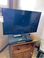 Front view of the 32 inch Samsung TV on a wooden surface with Magnavox DVD player and remote on top.