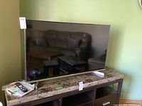 Front view of the Sharp 50" LED LCD TV on marble top with remote and manual visible