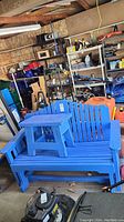 Blue painted wooden glider bench with a matching small wooden table placed on top. Visible scratches and paint wear.