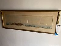Framed ocean wall art hung on a wall, showing sailboats and rocky shoreline.