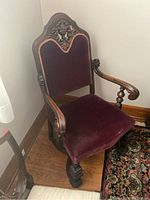 Front angled view of the Mohlhenrich carved wooden chair showing carved details, maroon velvet seat and backrest, and armrest design.