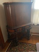 China cabinet with curved wooden doors and ornate carved legs, showing front and side views.