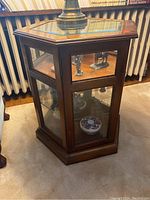 Front side and partial top view of the wooden octagon display table with glass panels and interior glass shelf, containing decorative items.
