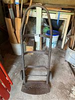 Front view of metal hand truck standing upright showing rust and bent cross piece.
