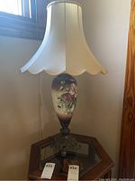 Full view of the lamp showing floral glass body, metal base, and beige scalloped lampshade