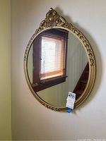 Full view of the oval mirror showing the gold ornate frame and the reflective surface mounted on a wall.