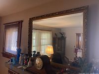 Full view of the large wall mirror reflecting part of a living room with furniture and lamps.