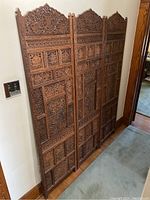 Full view of three carved wooden decorative panels with floral and leaf patterns, standing side by side against a wall.