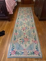 Full view of the runner rug laid on wood floor, showing blue background with floral design and beige border.