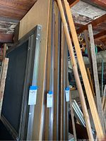Three folded 8ft tables with wooden tops and metal frames leaning against a wall in a garage, showing the tops and metal legs folded underneath.