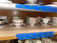 Porcelain vintage teacups and saucers with floral patterns on a shelf.