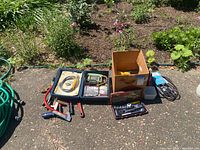 Full view of the lot set outdoors including power tools, clamps, wrenches, belts, and boxed socket sets.