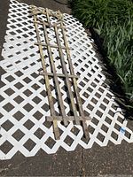 Large white plastic lattice trellis panel laid on ground with three weathered wooden trellises on top.