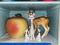 Shelf display showing McCoy peach cookie jar, porcelain cat figurines linked by chains, and vintage Nimbi fawn figurine.