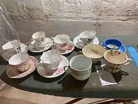 Nine vintage bone china teacups and saucers arranged on a table, showing variety of floral and gold patterns.