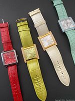 Front view showing four ladies square-face wristwatches with different colored leather straps in red, lime green, cream white, and aqua blue.