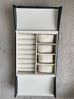 Open jewelry organizer box showing white interior with ring rolls and cushioned compartments.