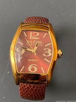 Front view of Joan Rivers Classics watch with gold-tone case and maroon dial showing numerals and hands.