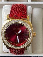 Joan Rivers Classic ladies quartz wristwatch with a red textured strap, gold-tone case with crystal-studded bezel, and a red dial with gold-tone markers.