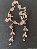 Close-up photo of necklace and earrings showing flower and leaf design with pink and translucent beads on silver-tone metal.