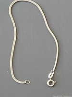 Photo of a flat linked sterling silver bracelet about 7 inches in length with a round spring clasp, laid out on a gray surface.