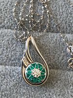 Close-up of necklace pendant showing green enamel floral design with white stone center.