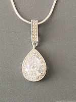 Close-up of the teardrop pendant with large faceted clear stone surrounded by smaller stones, hanging on a chain.