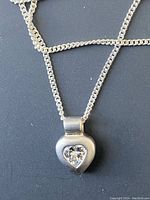 Close-up of silver necklace with heart pendant featuring a clear stone.