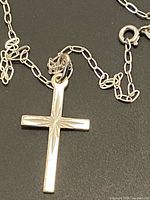 Silver necklace shown with a polished cross pendant that has a sunburst pattern engraving on the front.