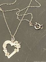 Close-up photo of sterling silver heart-shaped pendant with floral details on a silver chain necklace showing the pendant and the chain clasp.