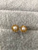 Front view of the pair of sterling silver stud earrings with yellow stones and pearl center, showing floral pattern.