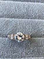 Close-up photo of sterling silver ring with a large round cubic zirconia center stone surrounded by smaller CZ stones on the band shown on a grey padded surface.