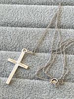 Sterling silver cross necklace laid on soft fabric background showing pendant and chain fully extended.