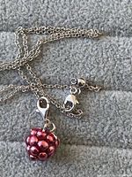 Close-up of sterling silver chain with red berry-shaped charm on a grey fabric background