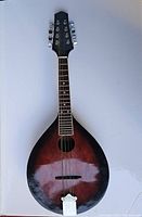 Full front view of the mandolin showing teardrop body shape, sunburst finish, sound hole, bridge, and tailpiece.