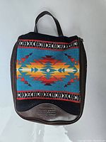Top view of Pendleton travel accessory bag showing colorful woolen fabric with geometric pattern and leather base with embossed logo.