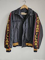 Front view of black vintage Caterpillar jacket with embroidery on sleeves and ribbed cuffs/hem.
