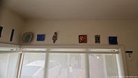 Wide angle view showing all seven wall art pieces mounted high on wall above window frame.