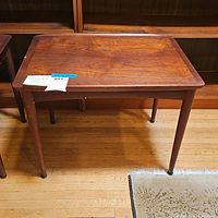 Front view of the small Danish wood table showing rectangular wood top, four round legs, and scratches on top surface and legs.