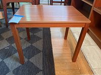 Front and angle view of the reddish-brown wooden MCM-style end table on a floor with part carpet and hardwood visible.