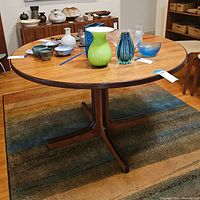 Full view of round teak pedestal dining table with accessories on top